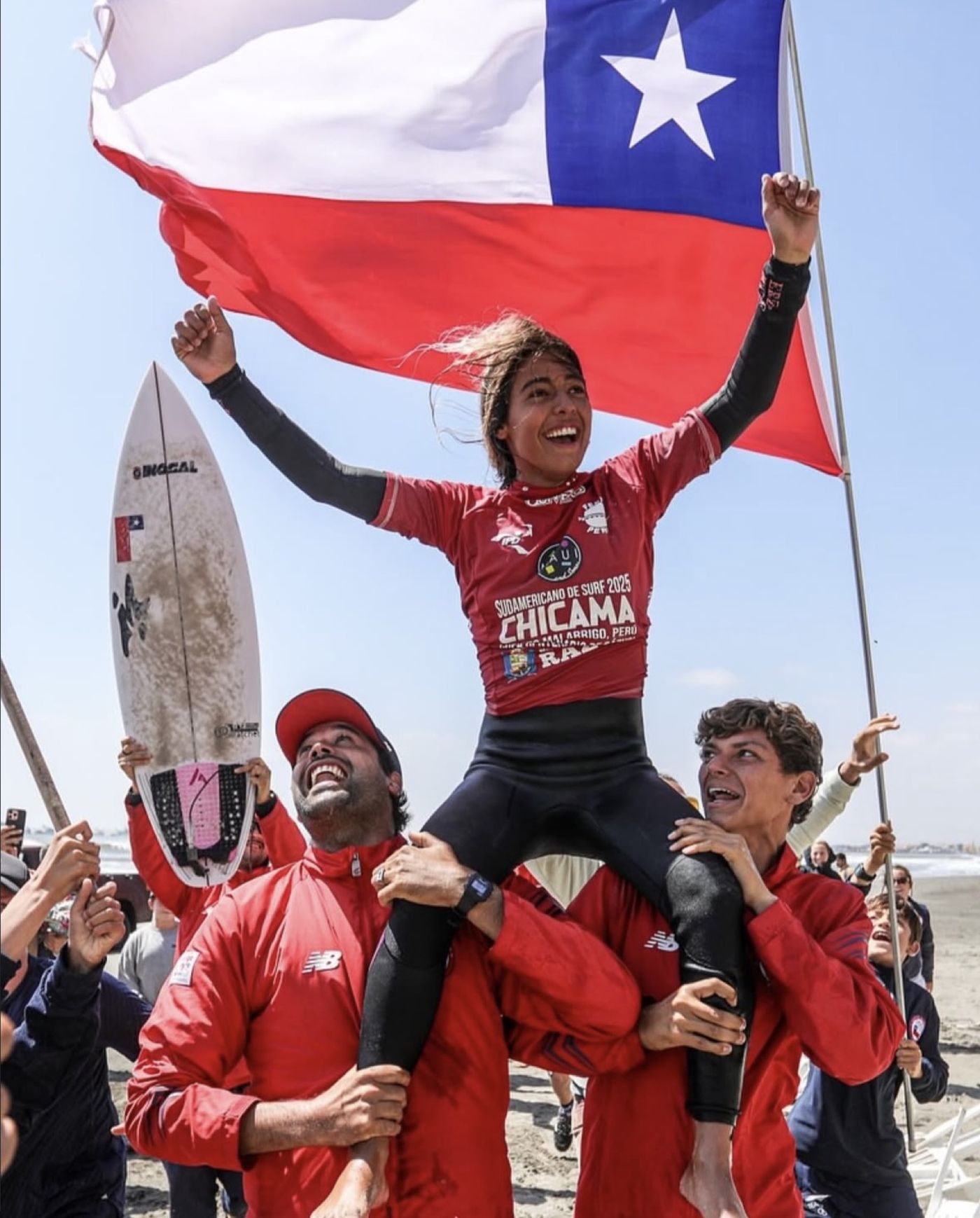 A surfer lifted on her team's shoulders under a Chilean flag