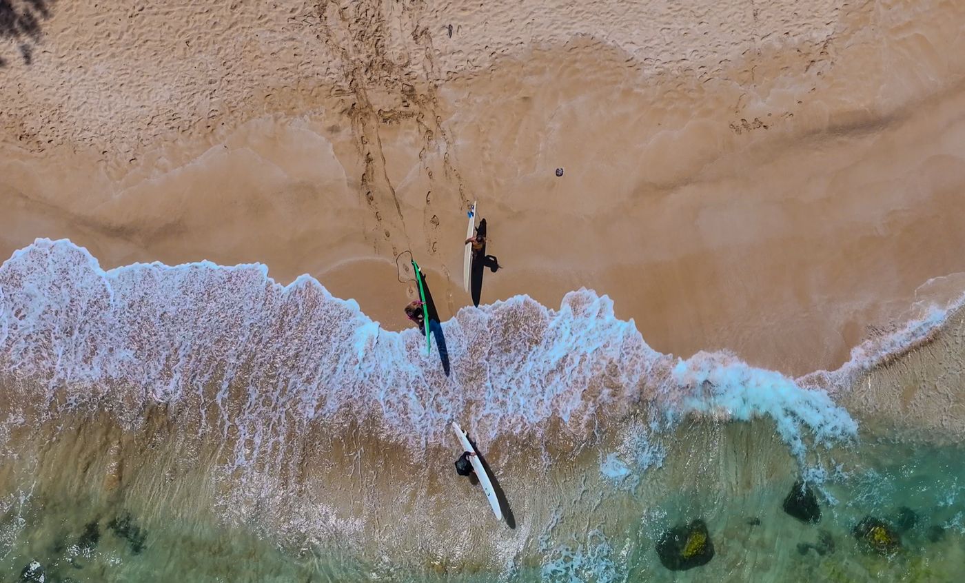Aerial view of surfers paddling out through white water